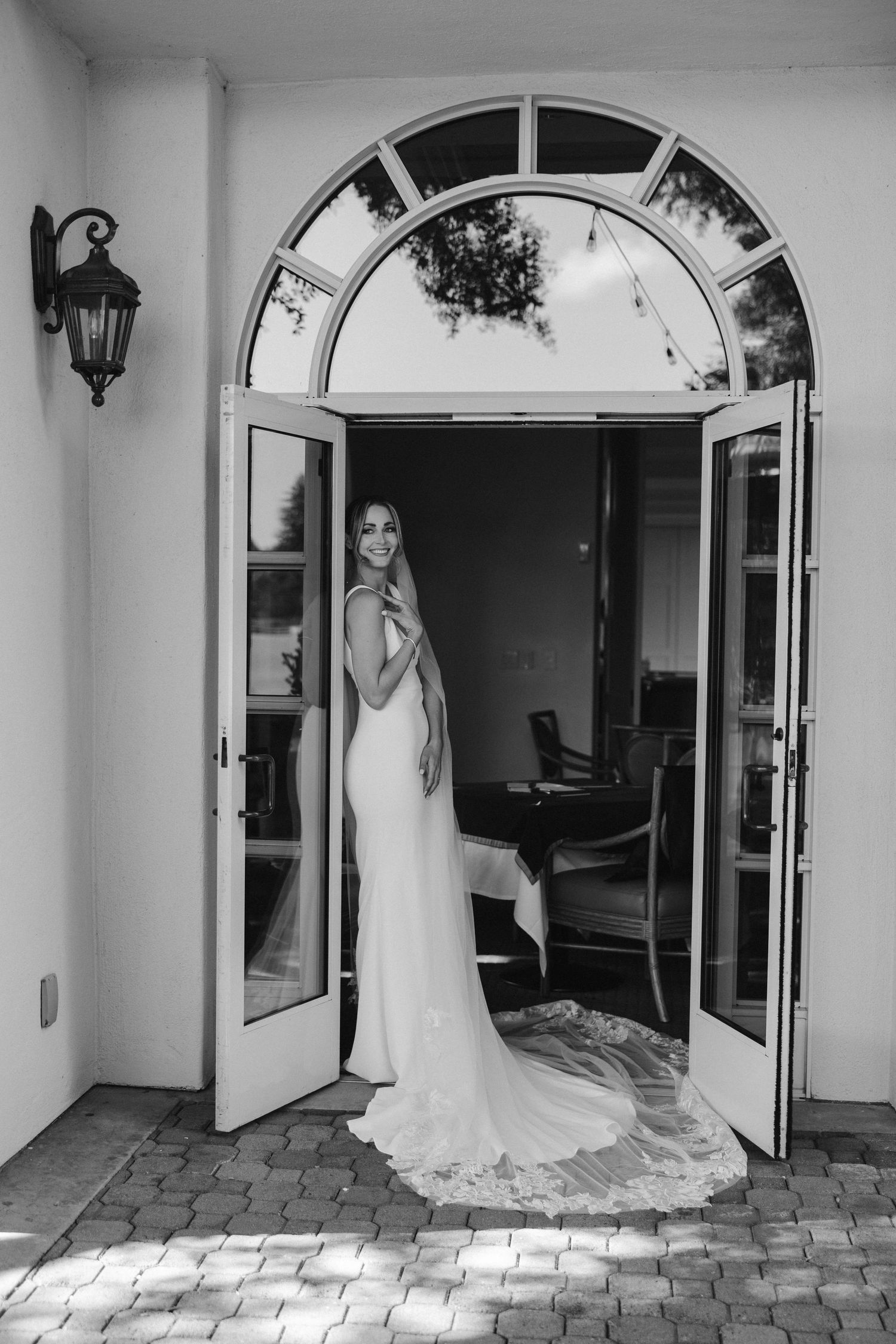 Black and white portrait of bridal silhouette in archway wearing fitted wedding dress with long train.