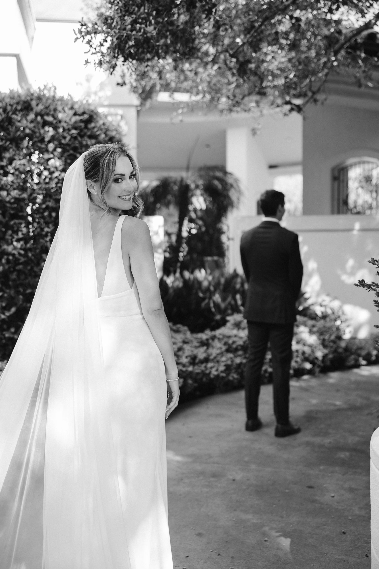 Black and white wedding photo showing bride and groom during first look in garden setting.