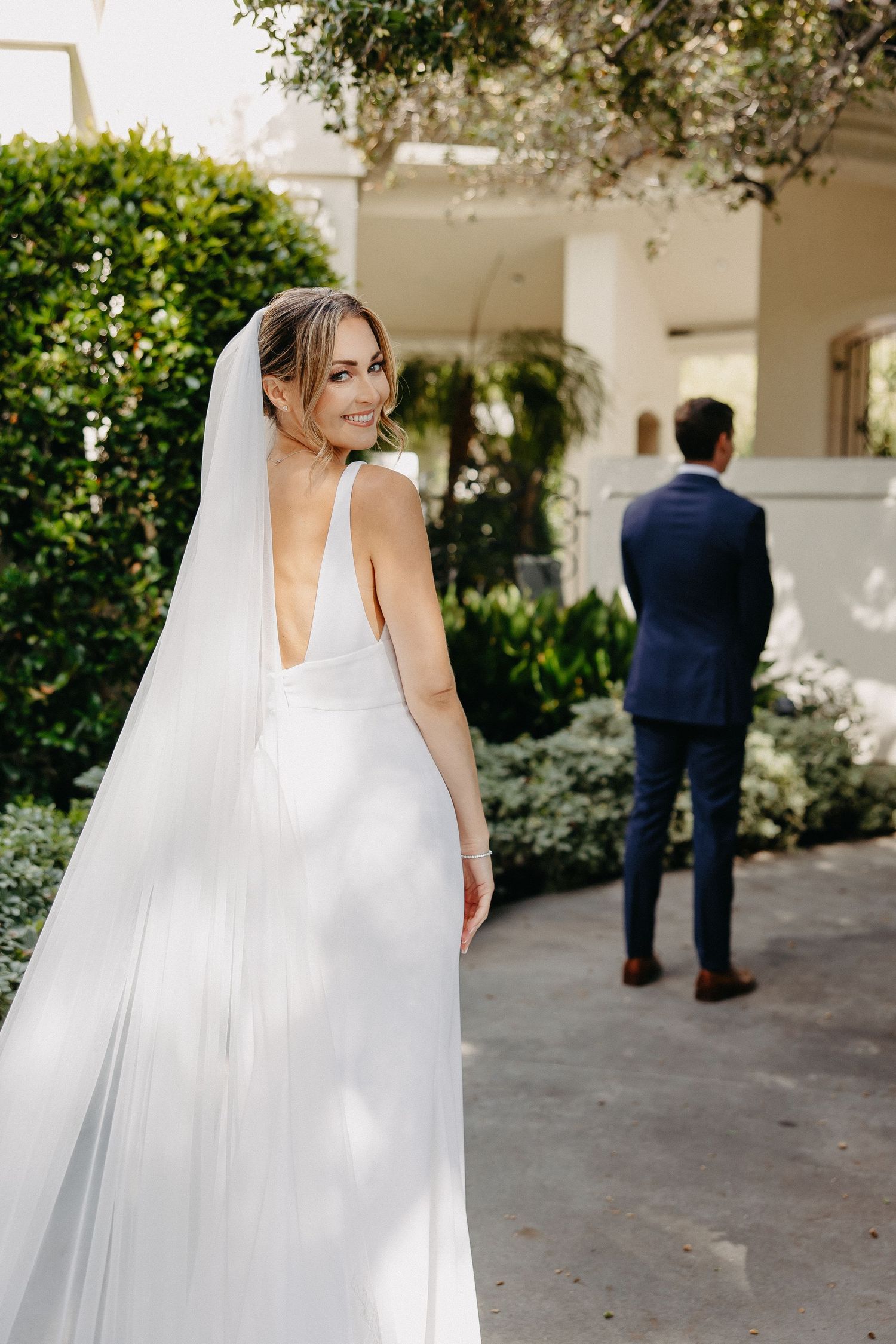 Elegant wedding dress with plunging back and flowing veil captured in garden setting.