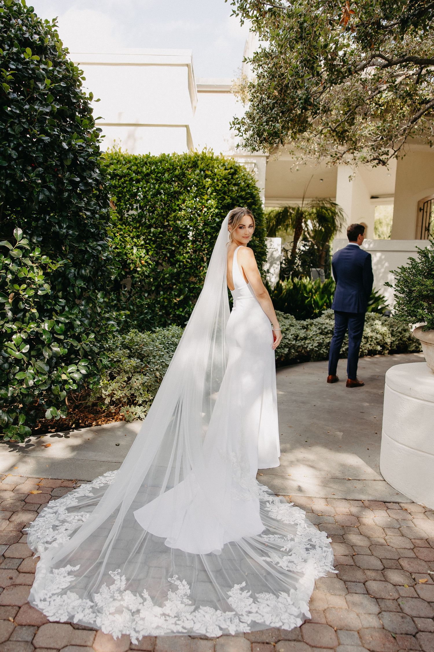 Full-length view of wedding gown with intricate lace-trimmed cathedral veil on garden pathway.