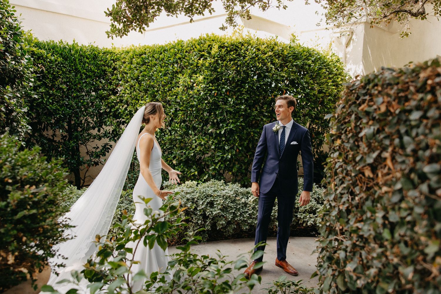 Romantic garden wedding photo showing couple amid lush greenery and hedges.