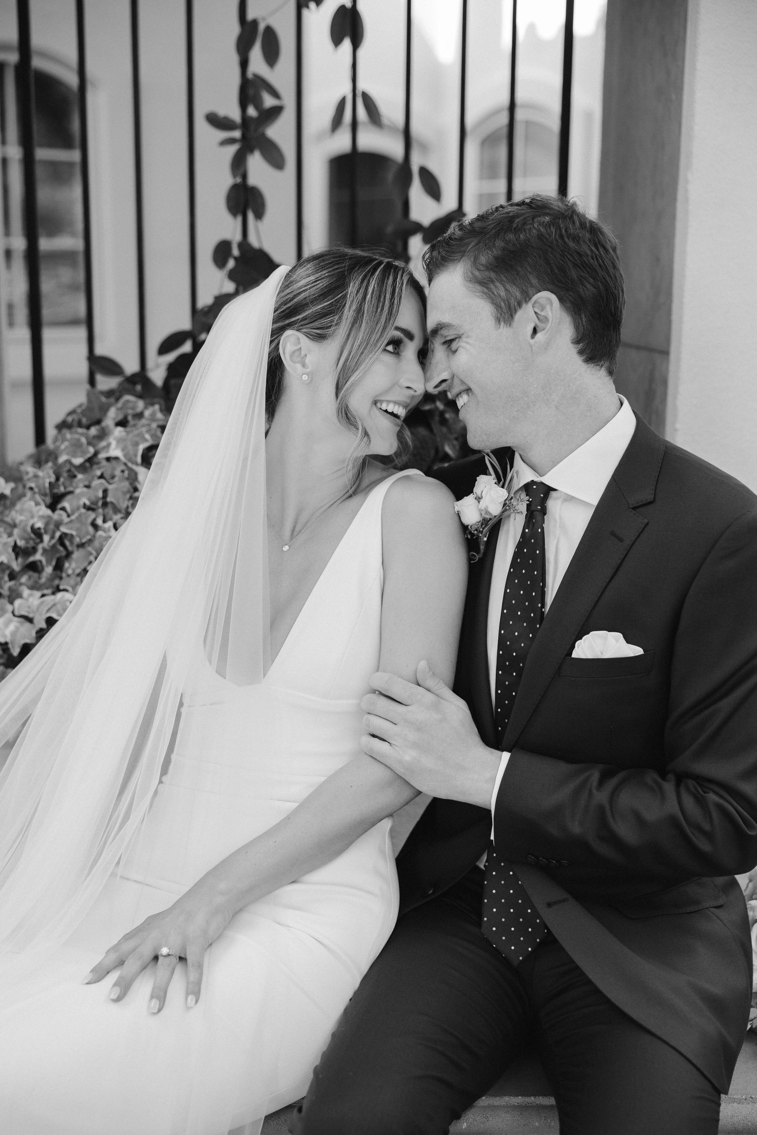 Black and white portrait of newlyweds sharing an intimate moment against an ornate iron gate.