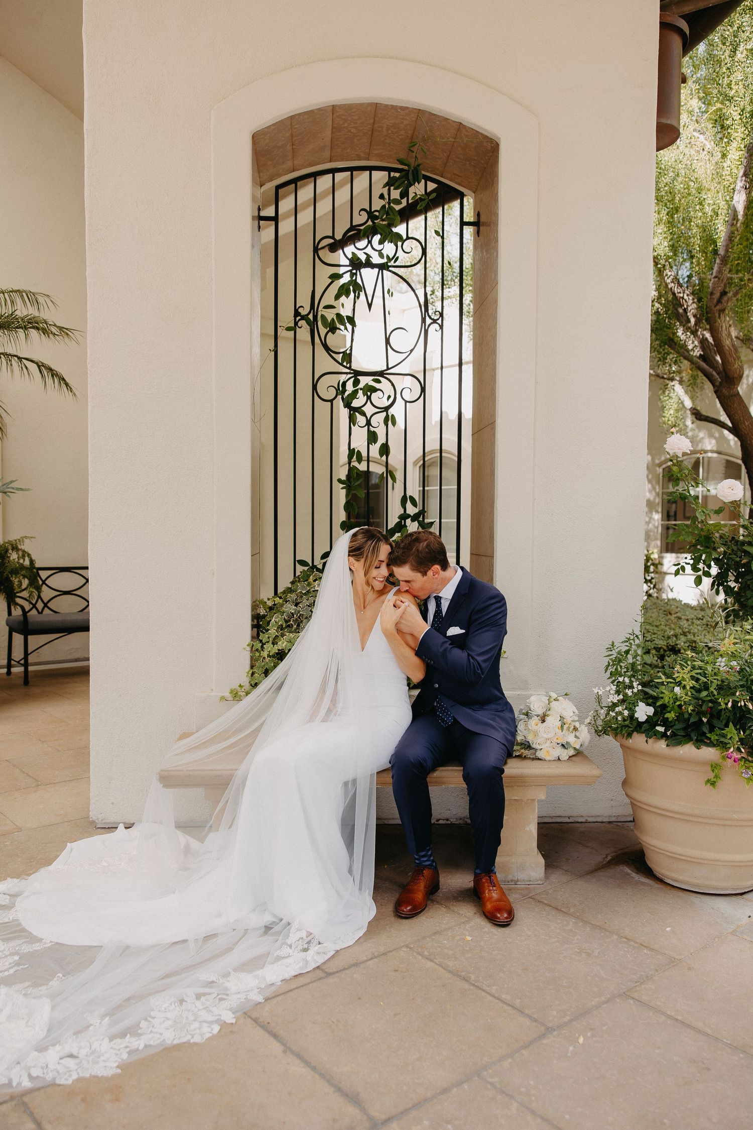 Wedding couple shares tender moment on stone patio beside ornate wrought iron gate.
