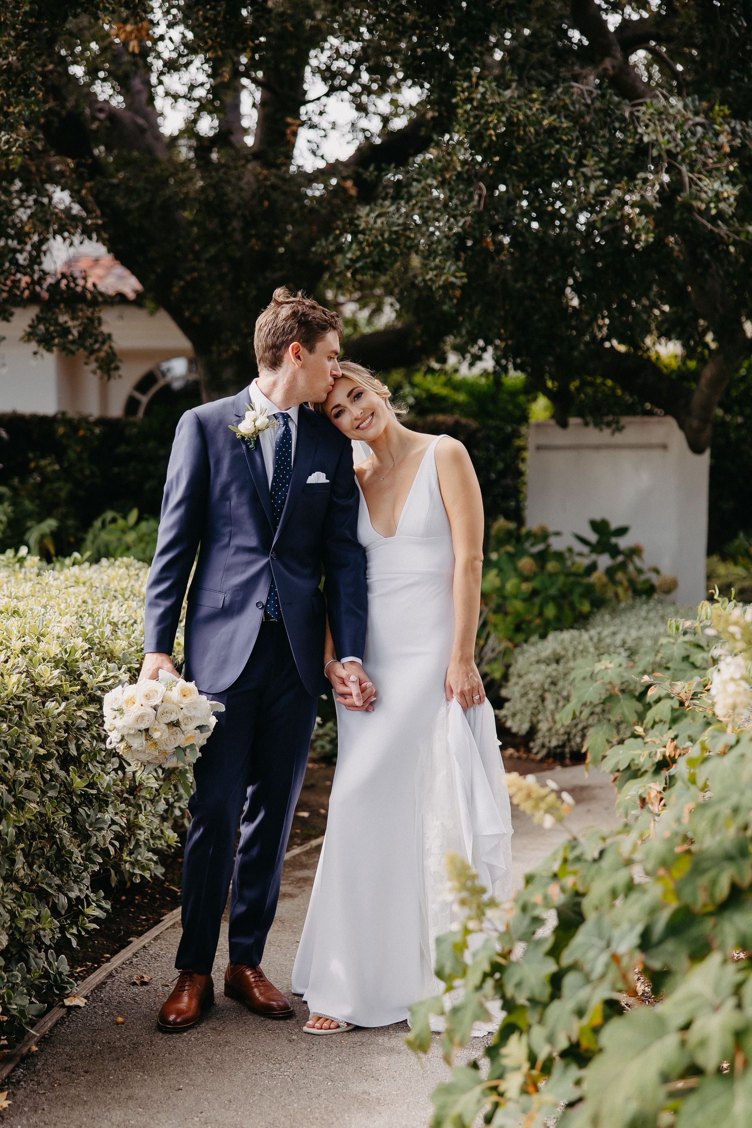 An intimate moment shared between newlyweds on a garden path surrounded by greenery.