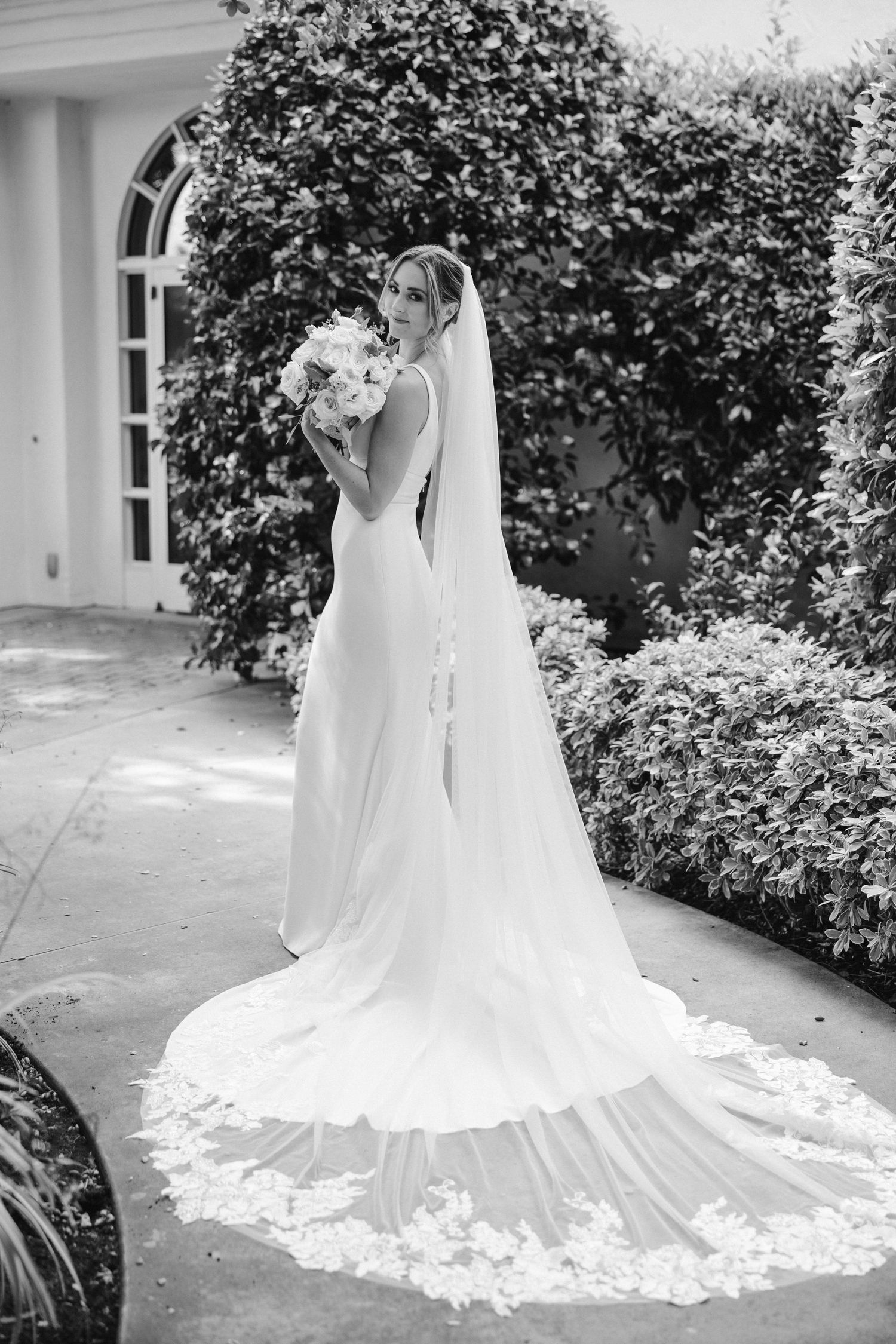 Elegant bridal portrait in black and white showing a flowing cathedral length veil and white bouquet.