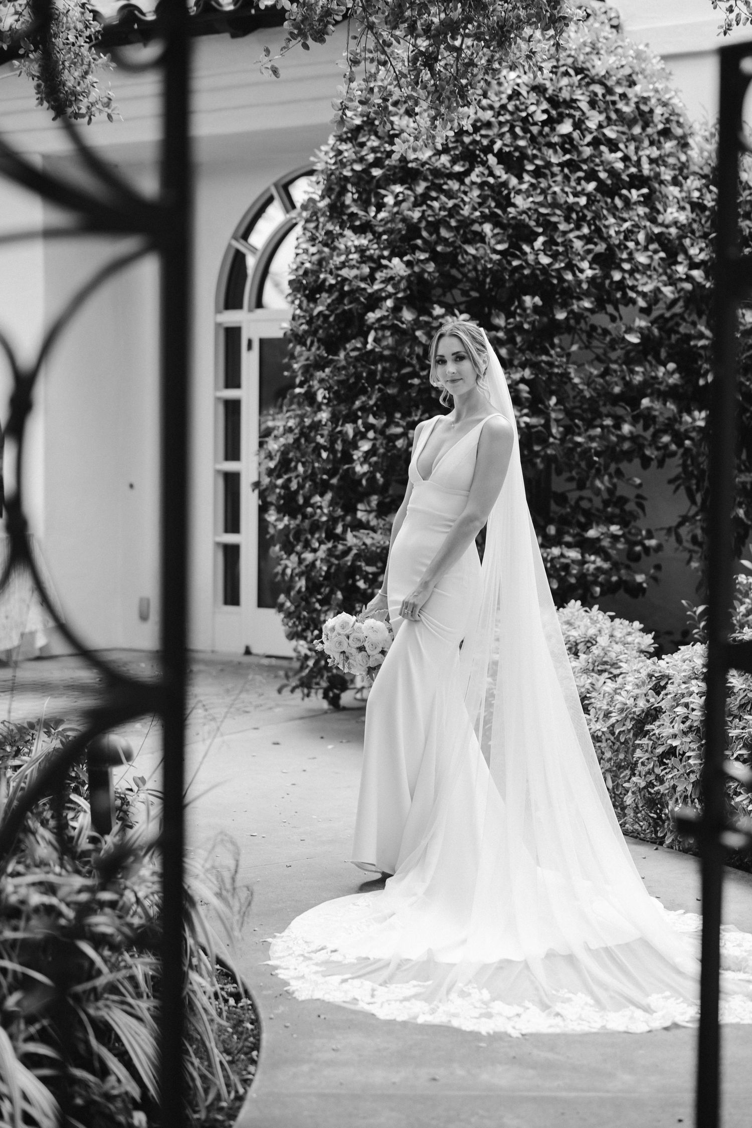 Classic black and white bridal photo featuring long train wedding dress in courtyard setting.