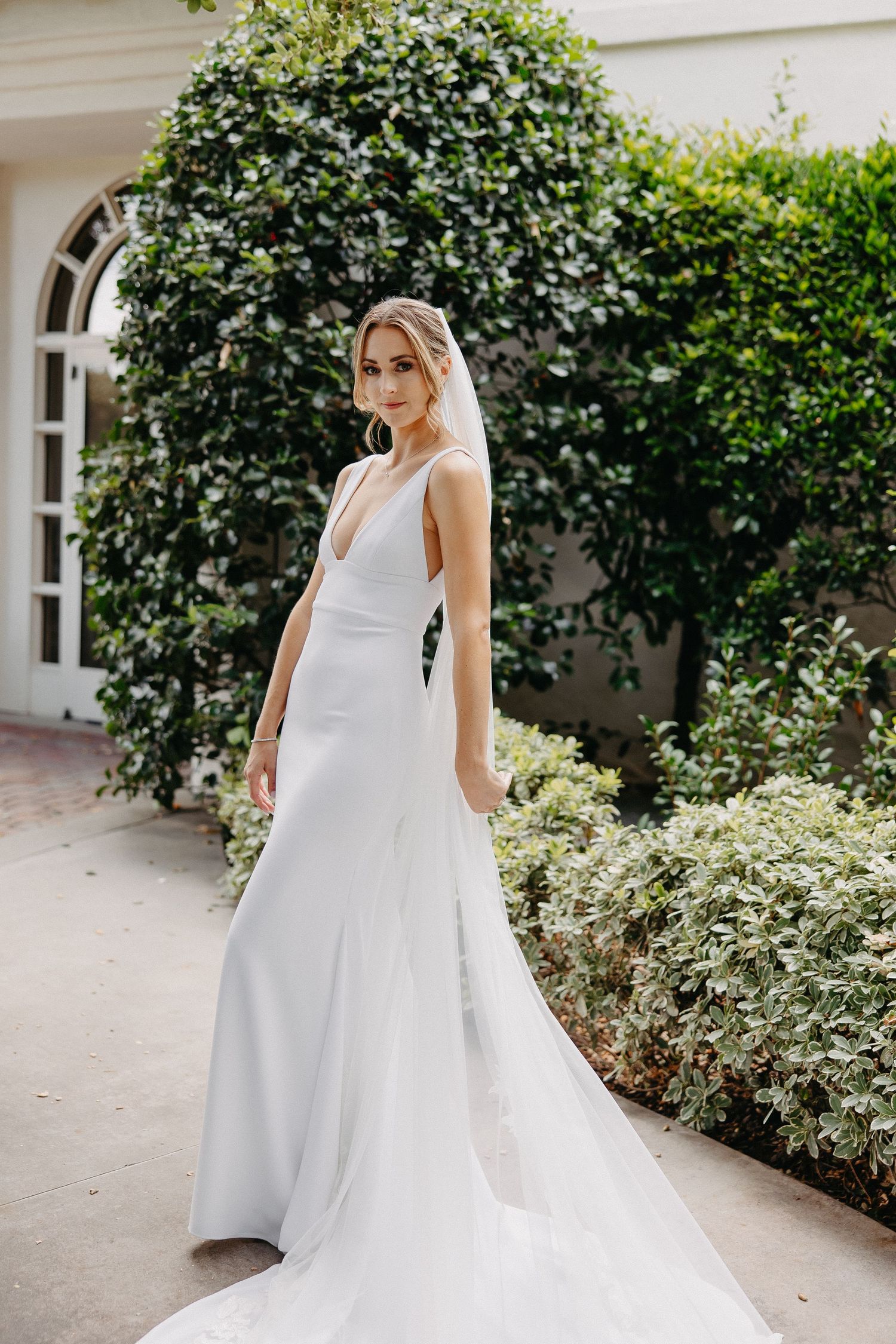 Modern wedding dress with clean lines and flowing train photographed in garden courtyard.