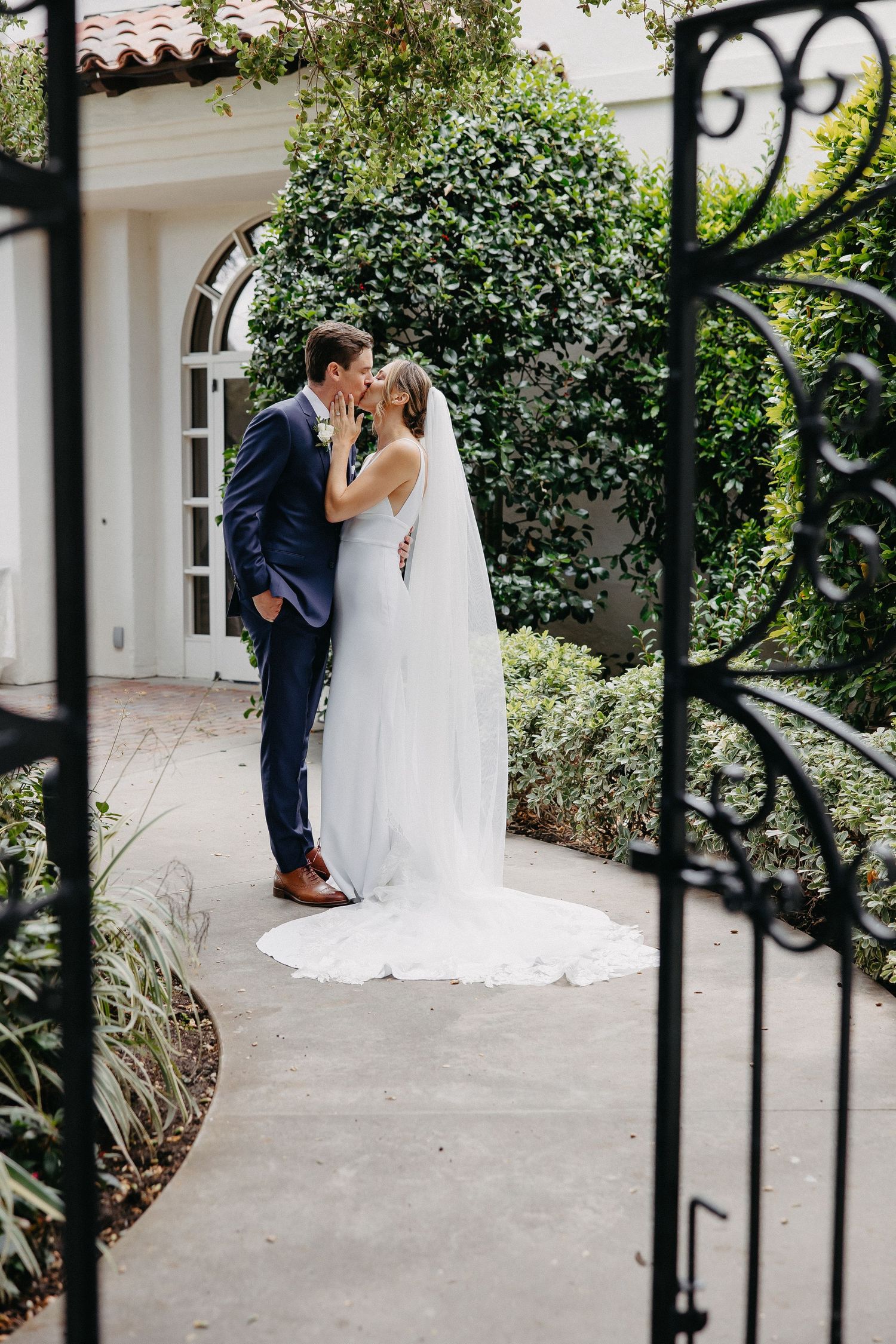 Intimate wedding moment captured through decorative iron gate in garden setting.