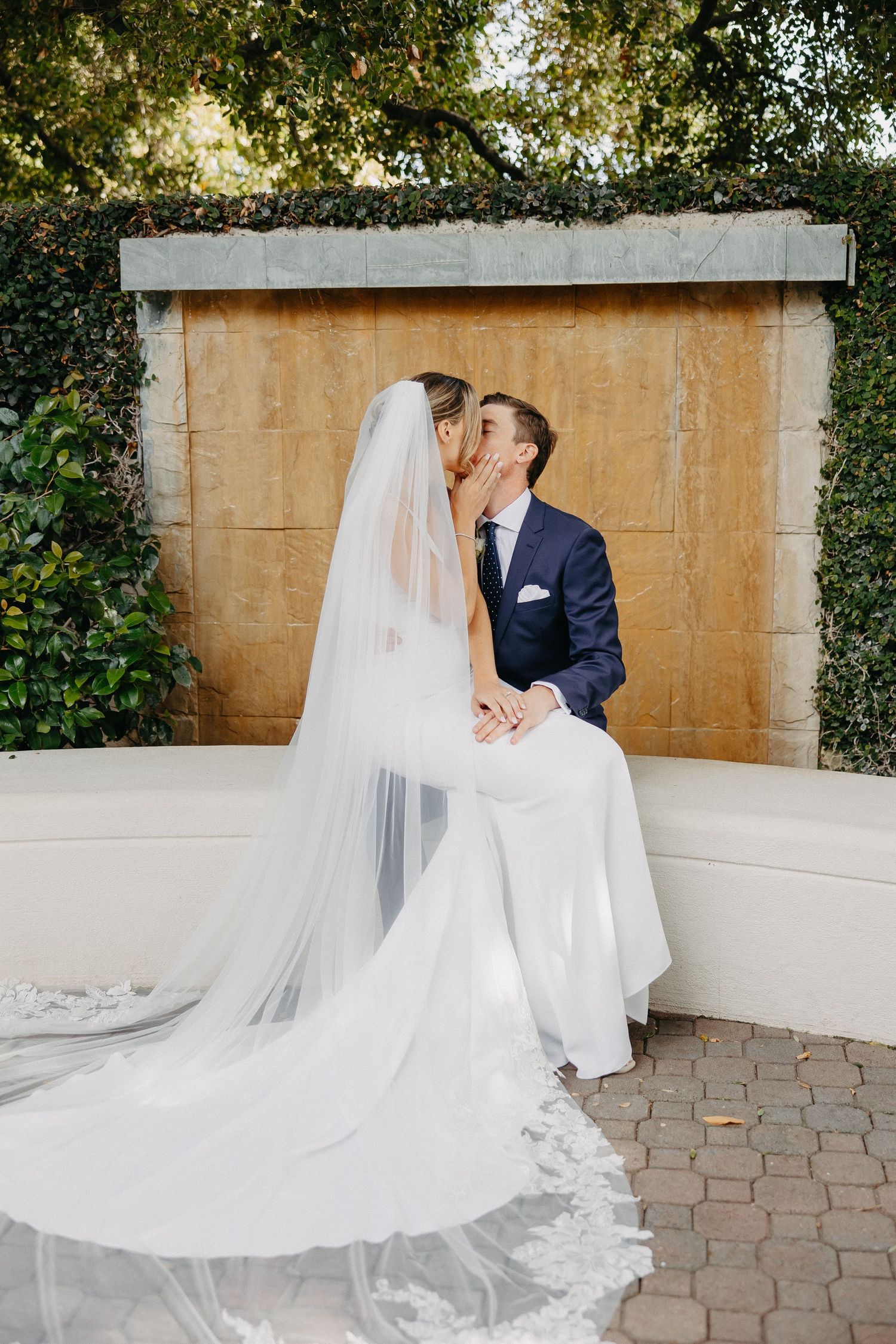 Wedding couple sharing an intimate moment on a stone bench with a long flowing veil.