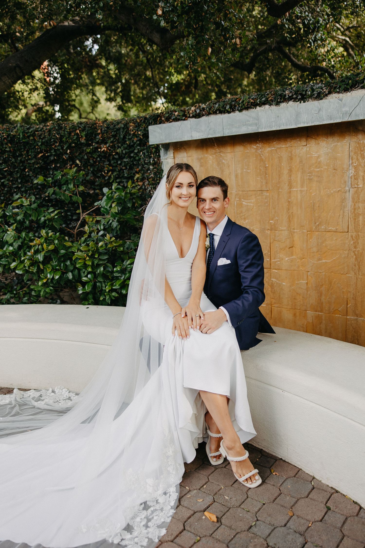 Newlyweds posing together on an outdoor bench with a dramatic cathedral veil.
