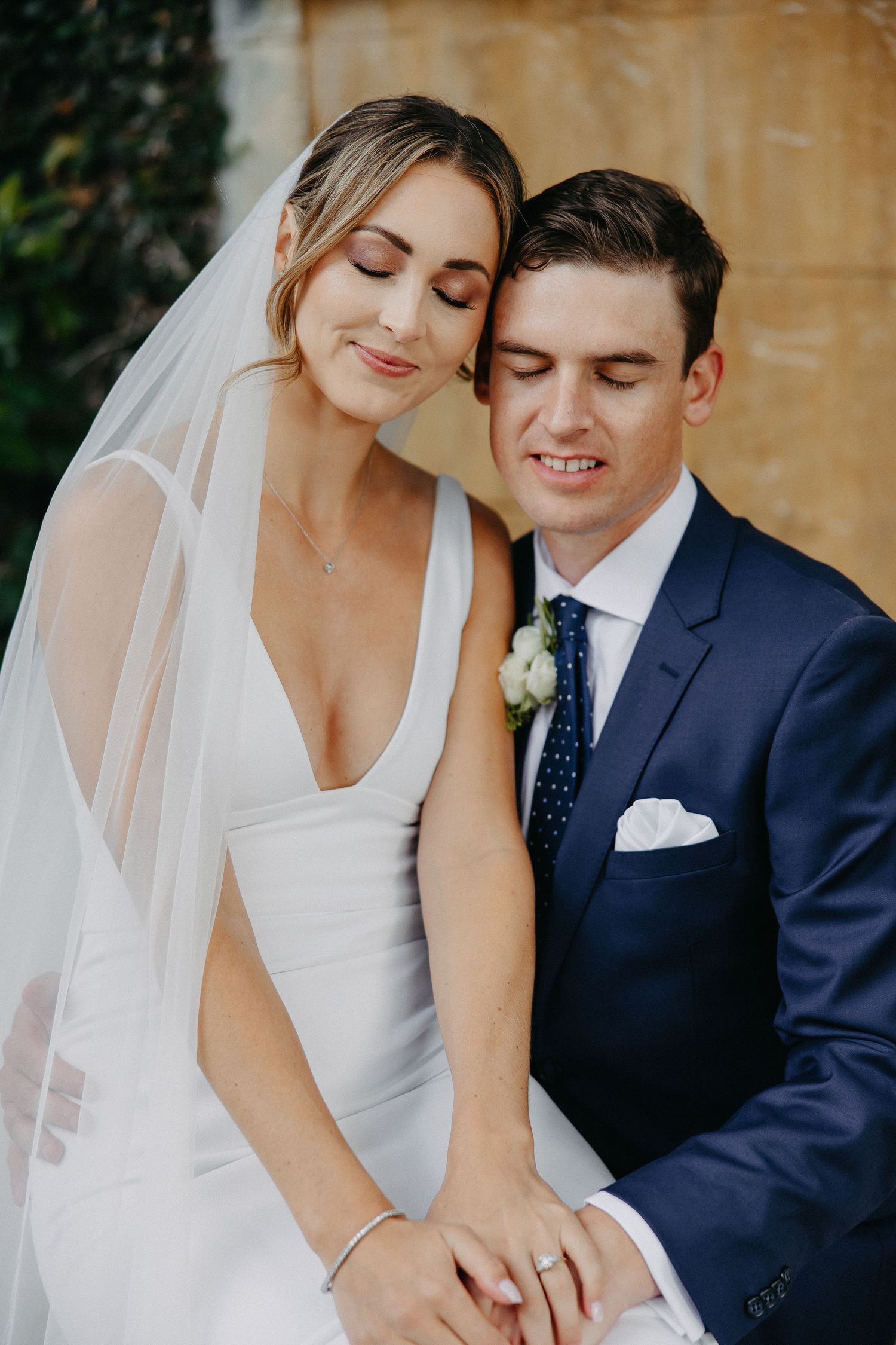 Romantic wedding portrait against a beige wall surrounded by greenery.
