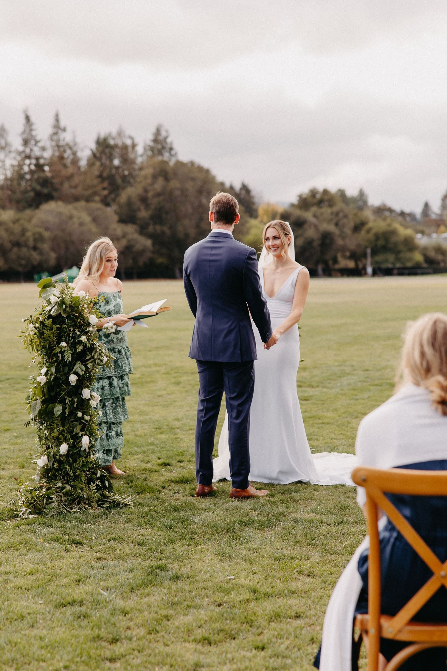 Outdoor wedding ceremony setup with floral arch and guests seated on wooden chairs.