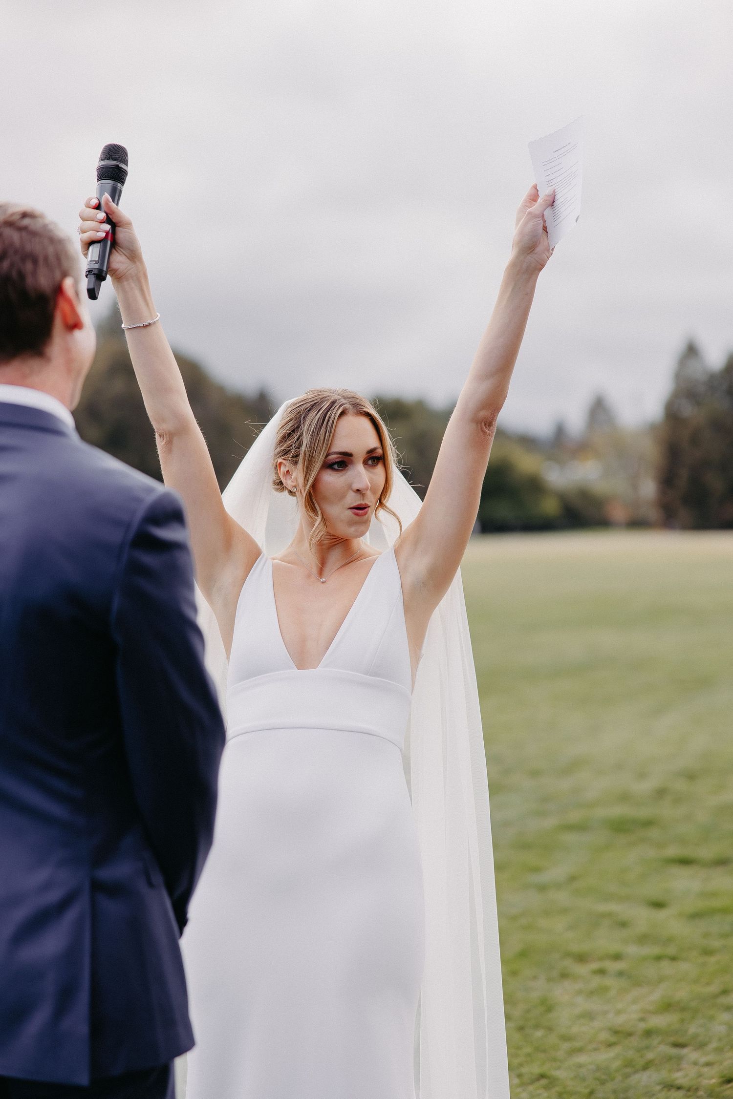 Joyful bride raises her arms in celebration during outdoor wedding ceremony.