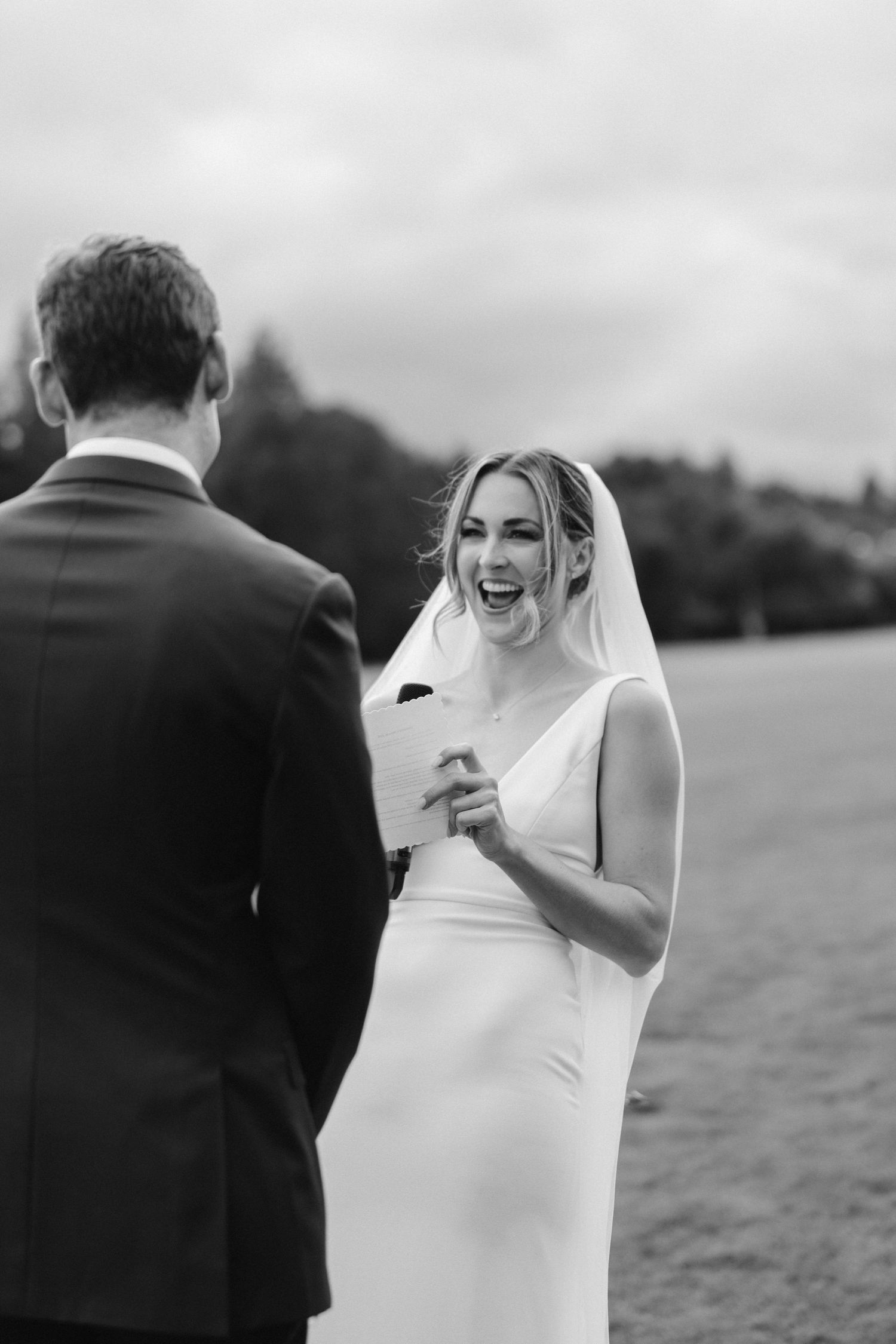 Black and white photo of a laughing bride during wedding ceremony exchange.