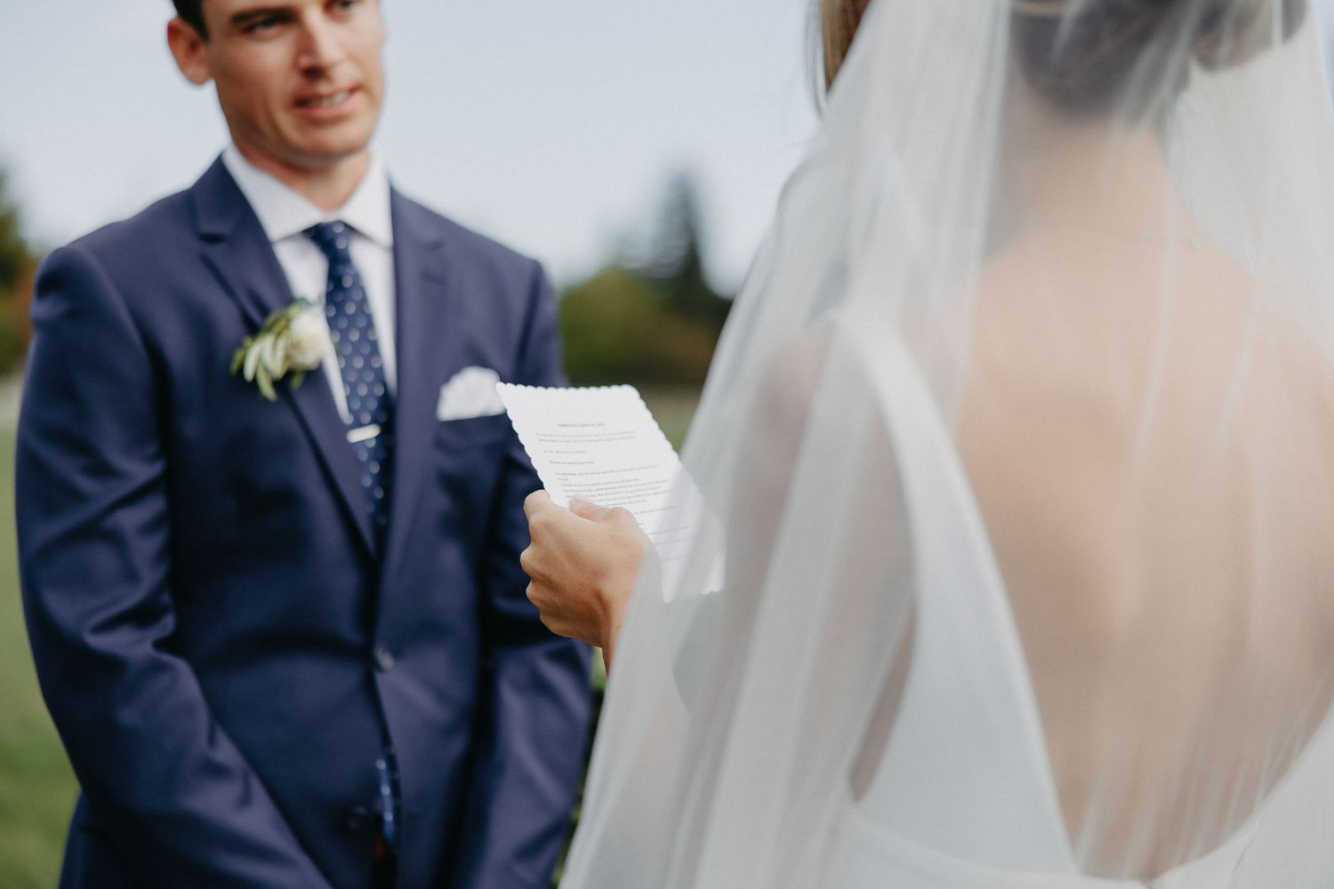 Close-up of couple exchanging vows at outdoor ceremony with groom reading from paper.