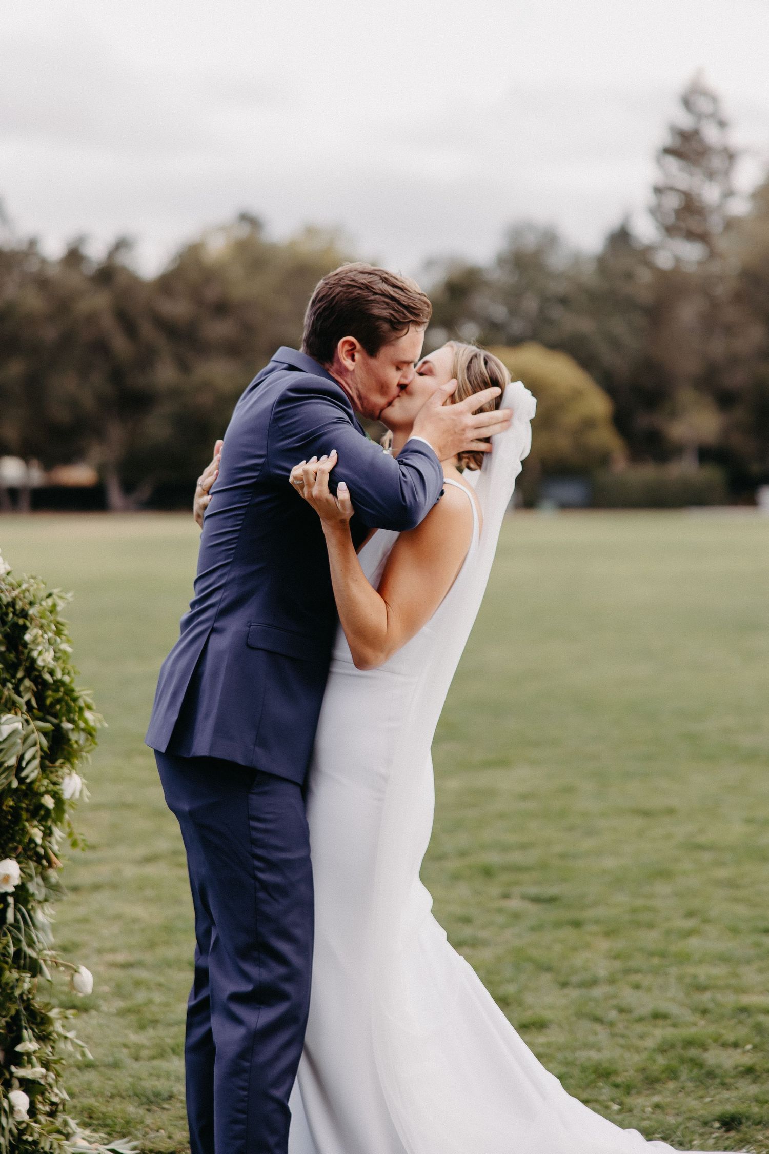 Intimate wedding moment as couple shares their first kiss surrounded by greenery.