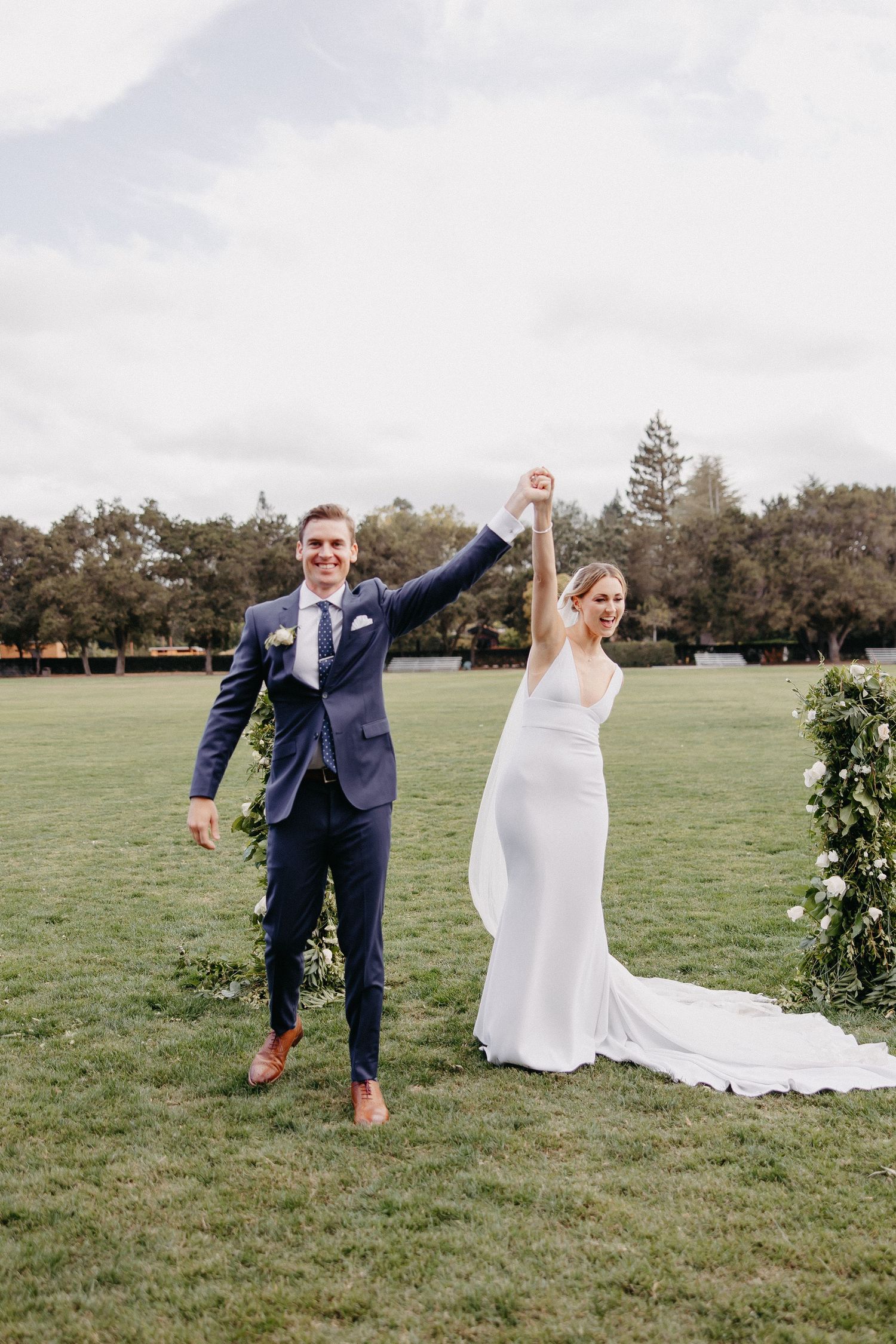 Newlyweds celebrate with raised hands on their wedding day in an outdoor setting.