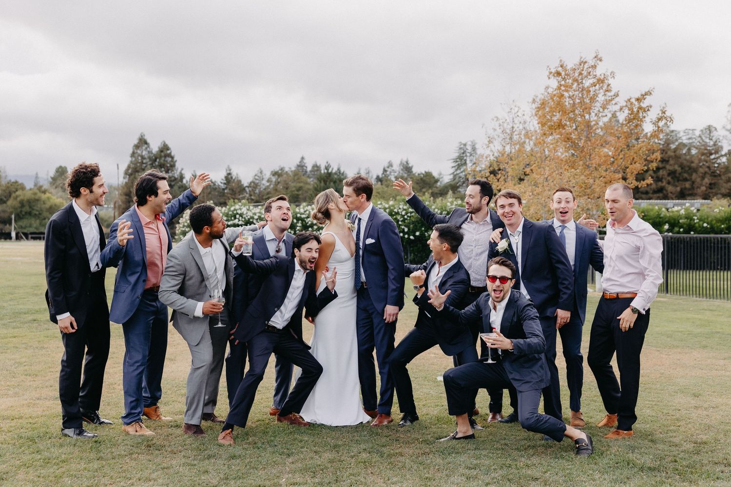 Wedding party posed outdoors on grass with bride and groomsmen in navy suits.
