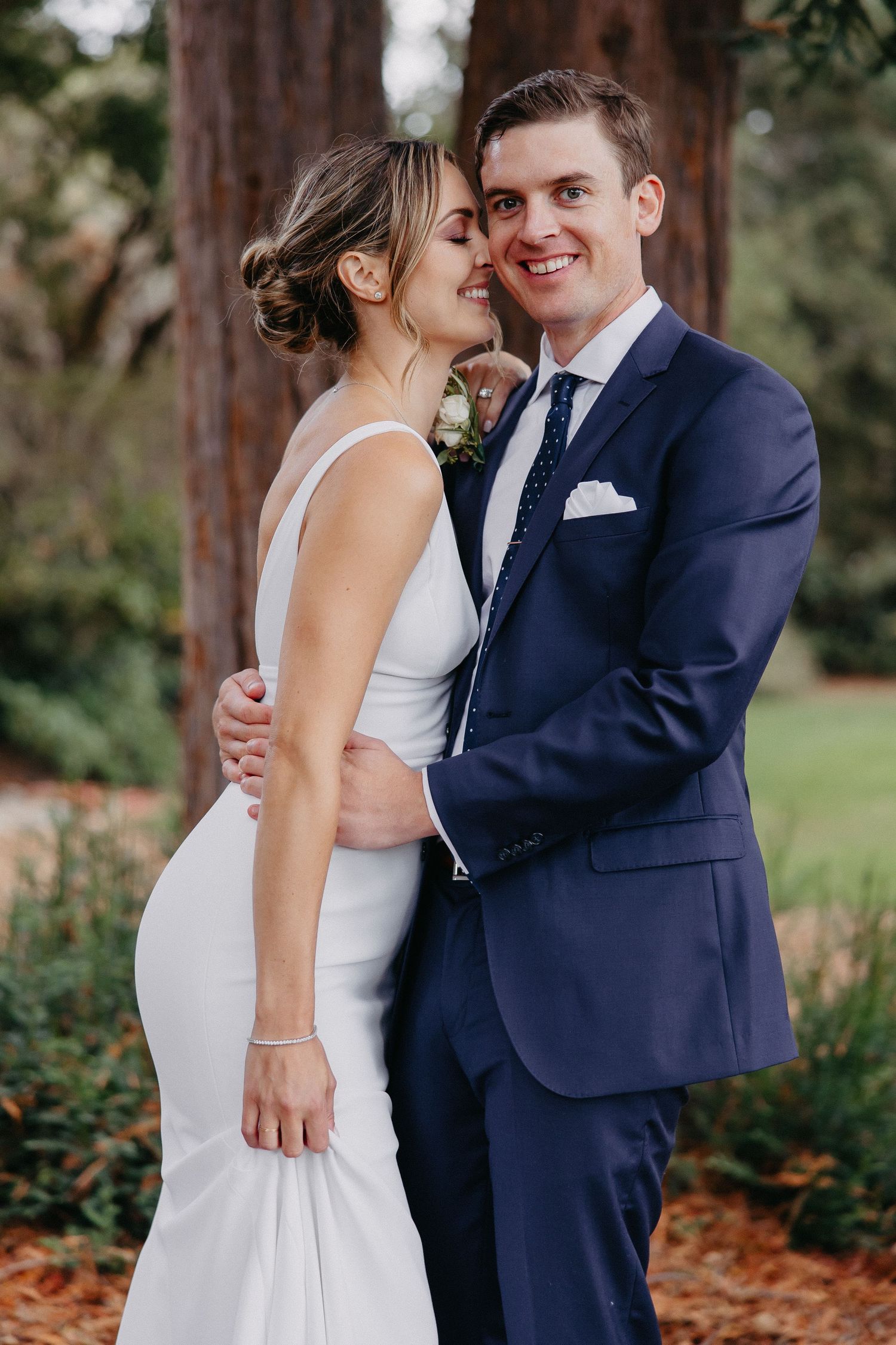 Intimate wedding portrait of couple in formal attire standing among redwood trees.