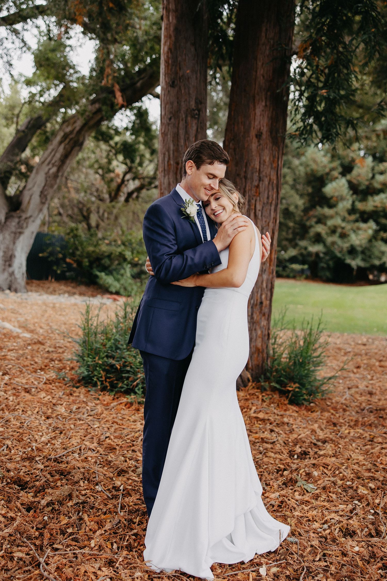 Romantic full-length portrait of wedding couple embracing among redwood trees.