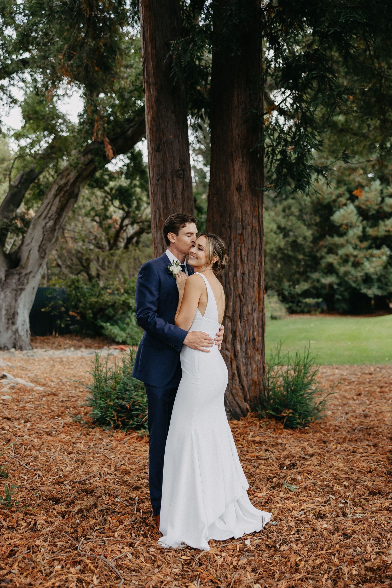 Couple shares intimate moment between towering redwood trees in an outdoor forest setting.