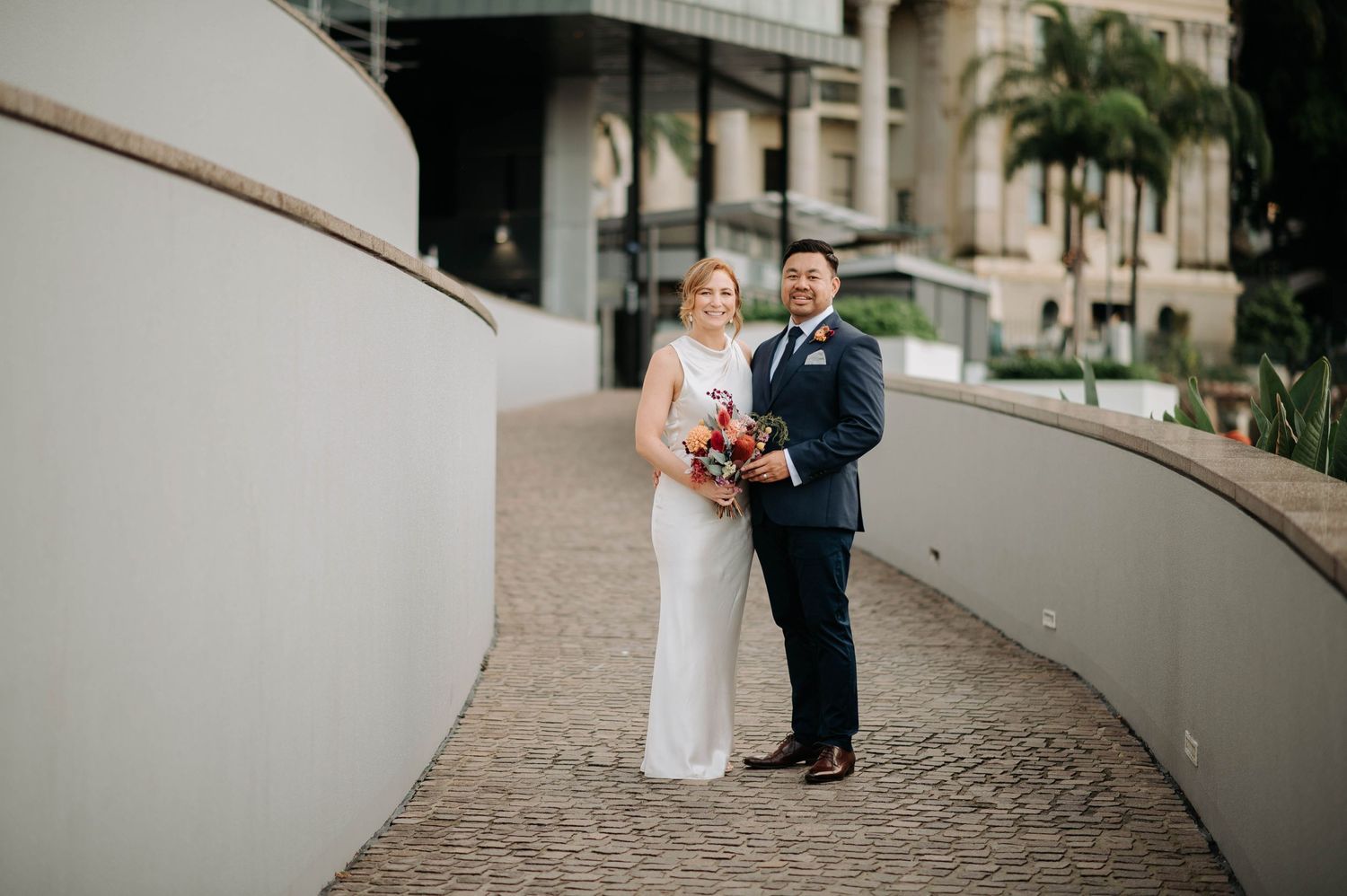 A couple poses together on a curved walkway during their wedding photoshoot.
