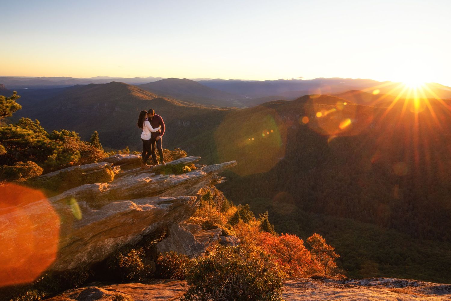 Mountain landscape at sunset with sun star bursting over distant ridges and valleys.