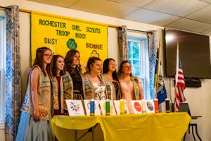 Girl Scout troop members standing behind yellow-draped table during formal ceremony.