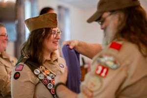 Girl Scout members in uniform with patches and badges interacting during a ceremony.