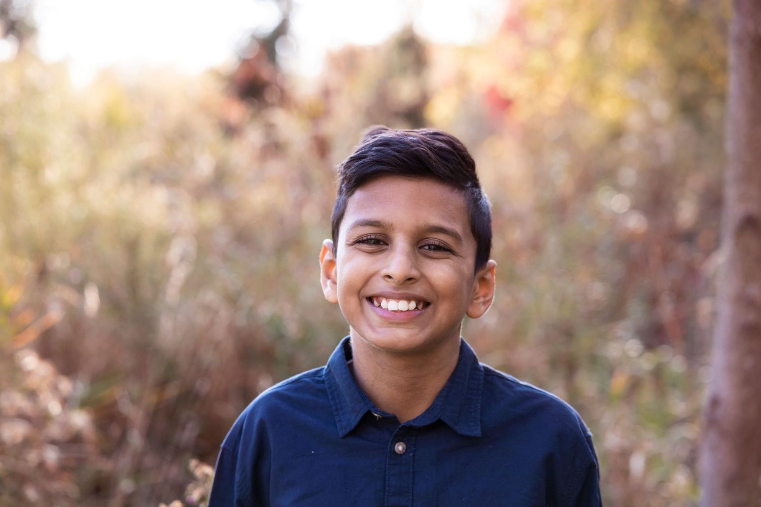 Young person in navy polo shirt smiling against blurred autumn background.