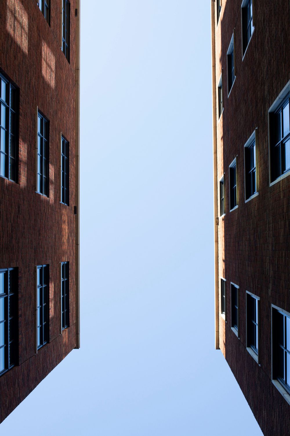 Modern brick building facade with blue windows photographed from below against clear sky.