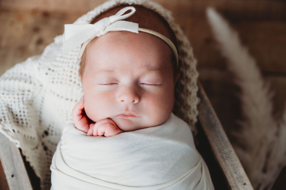 Sleeping newborn baby wrapped in white swaddle on textured backdrop.