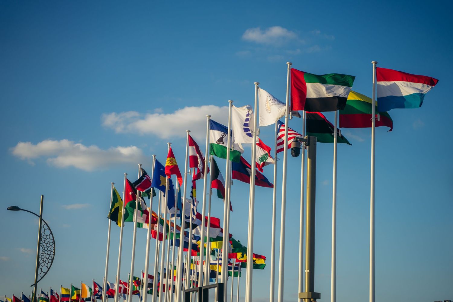 Row of international flags from various countries flying against a bright blue sky.
