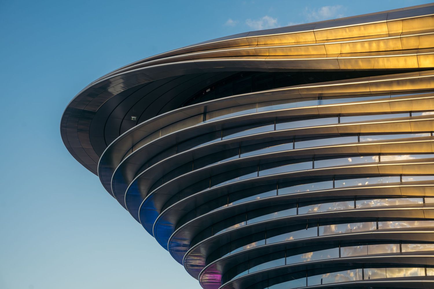 Modern curved architectural building exterior with layered metal panels at golden hour.