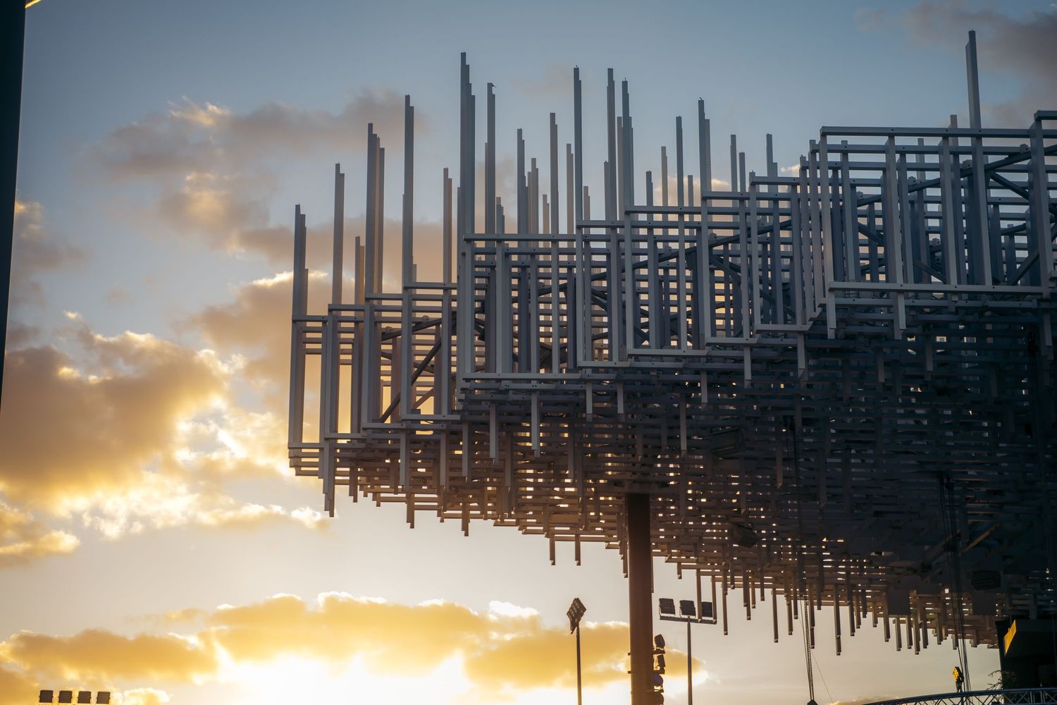 Steel construction framework silhouetted against a dramatic golden sunset sky at a building site.