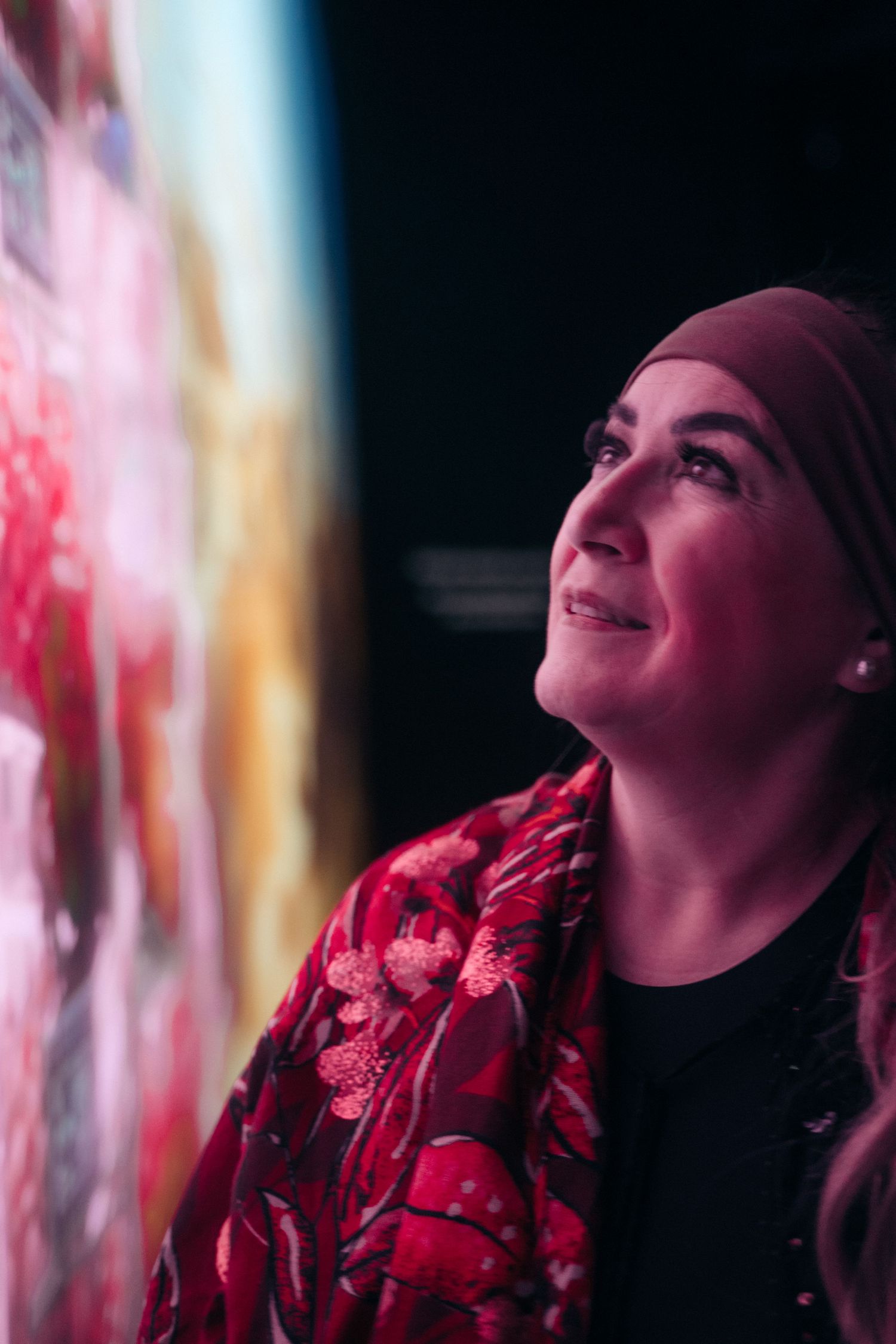 A woman in a hijab gazes upward at a vibrant colorful display inside an exhibition pavilion.