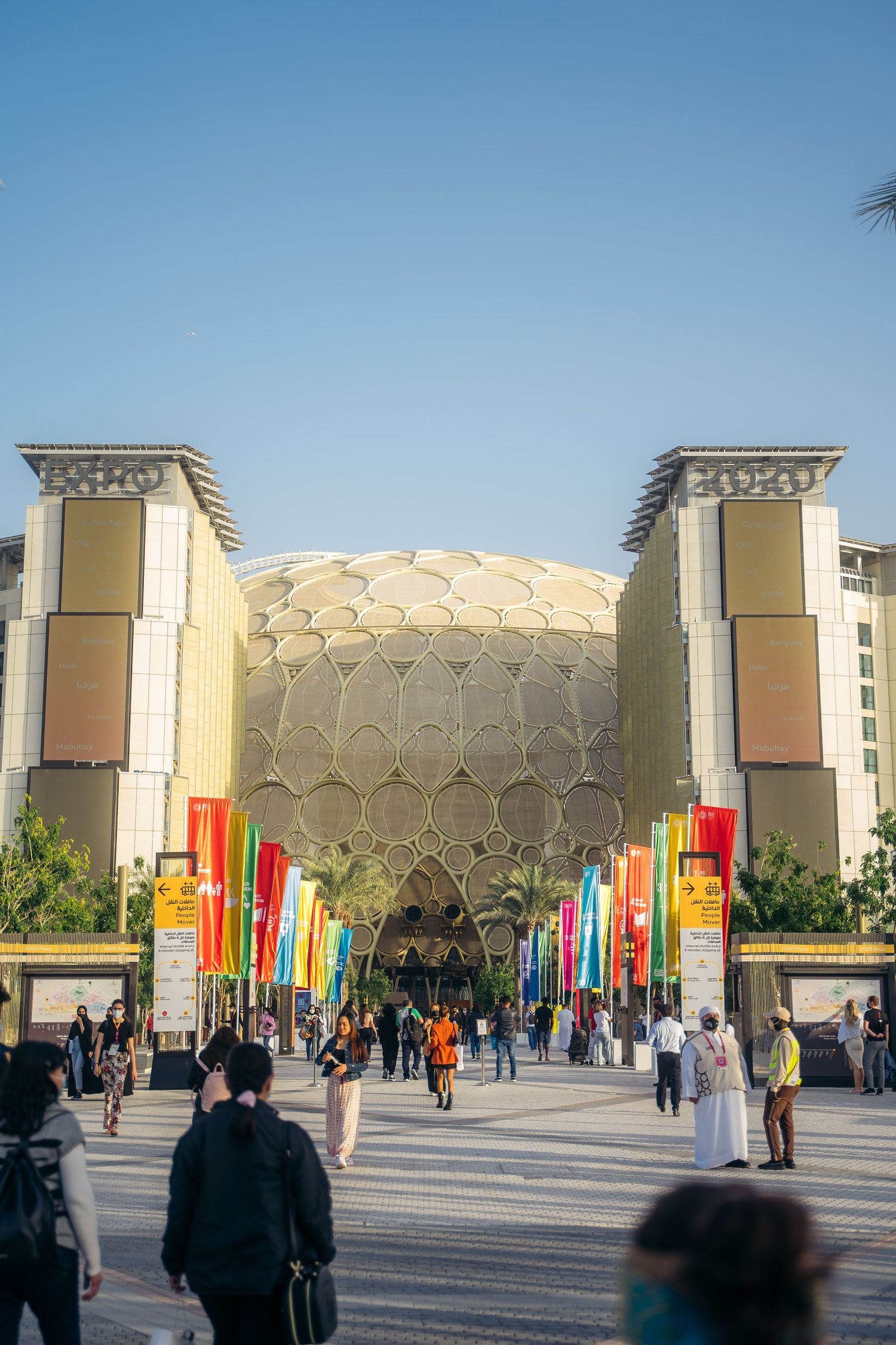 Golden dome of Al Wasl Plaza at Expo 2020 Dubai flanked by colorful flags and visitors.