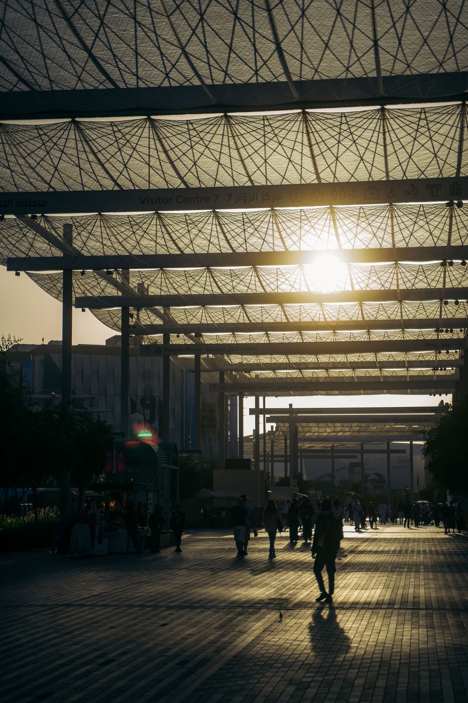 Silhouettes of people walking under a geometric lattice canopy at sunset in Dubai.