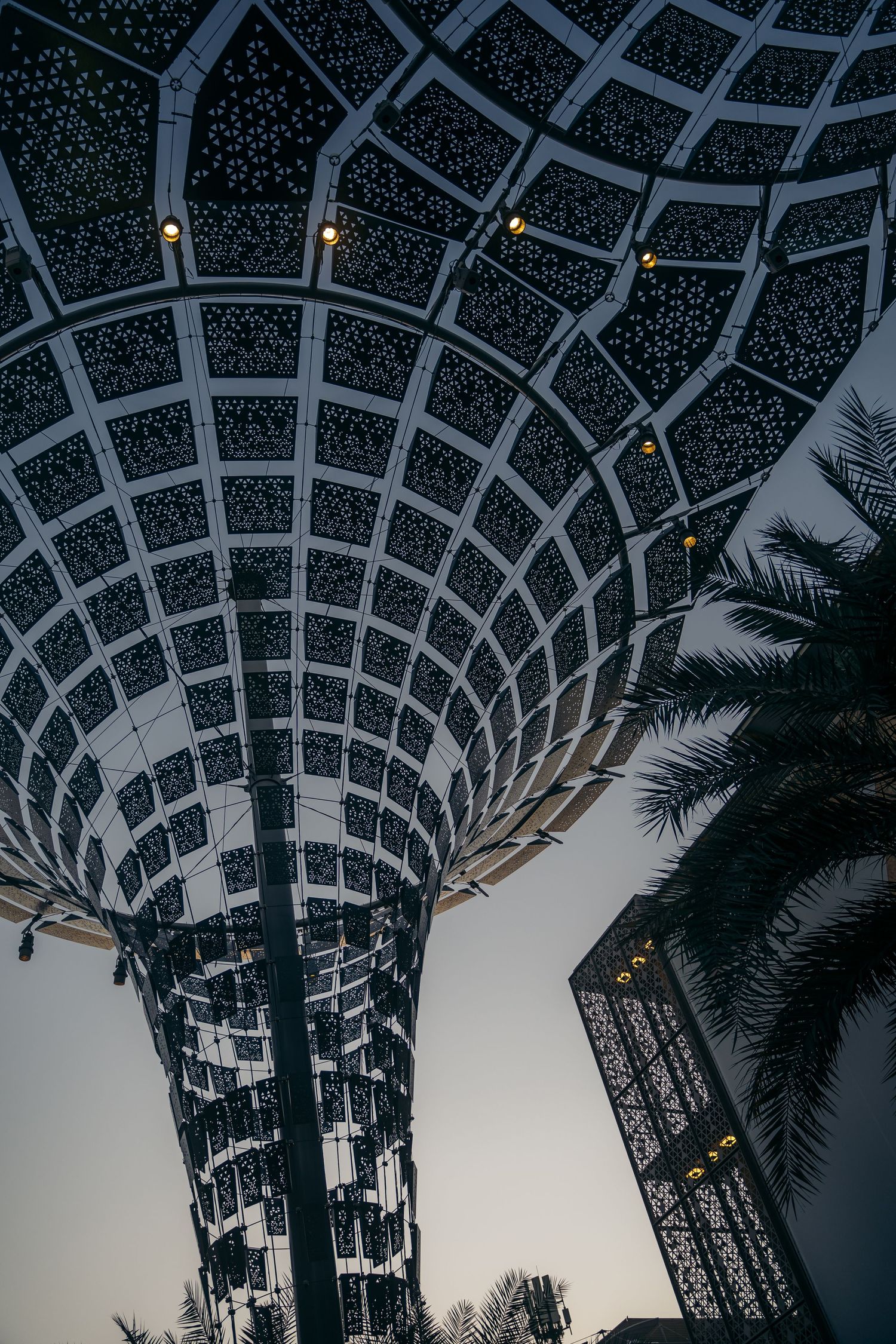 Illuminated futuristic tower structure with geometric patterns at dusk at Expo 2020 Dubai.
