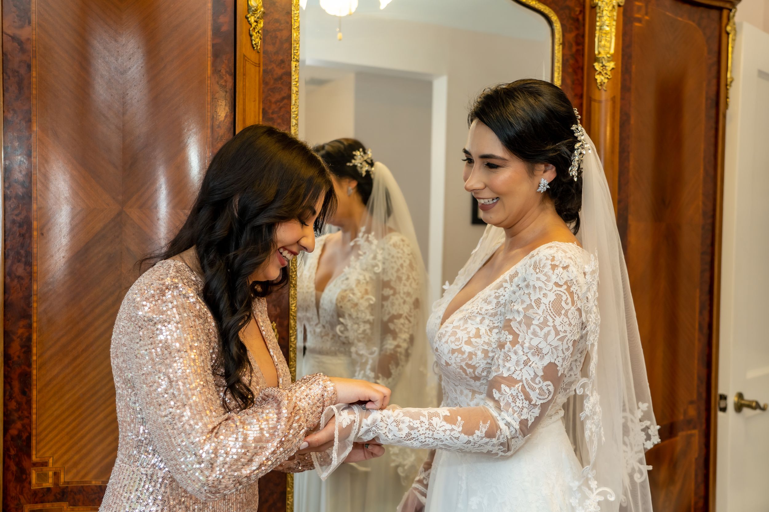 Two people working together to prepare a bride's white lace wedding dress and veil.