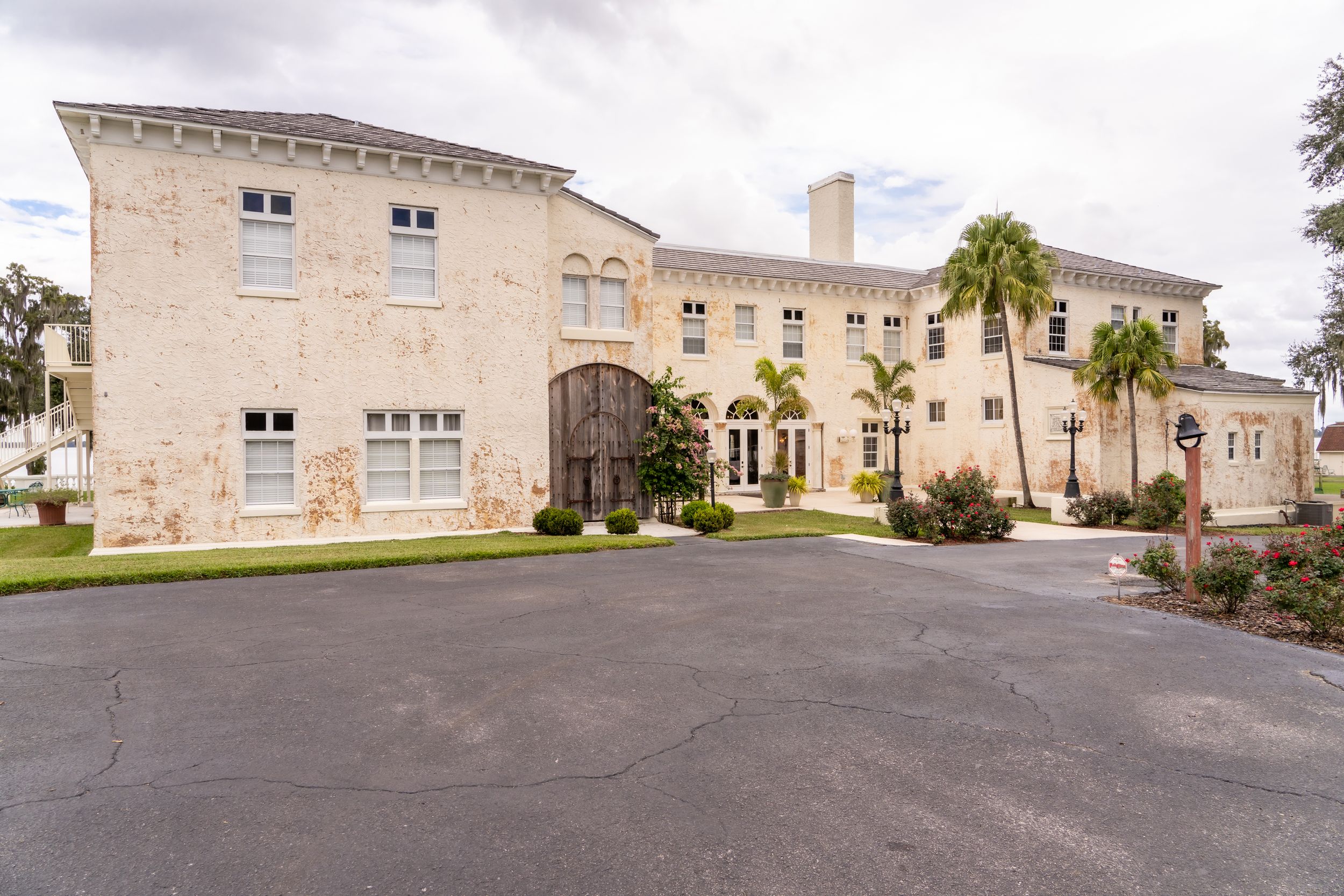 Historic stone mansion with palm trees and curved driveway entrance showcasing elegant Mediterranean architecture.