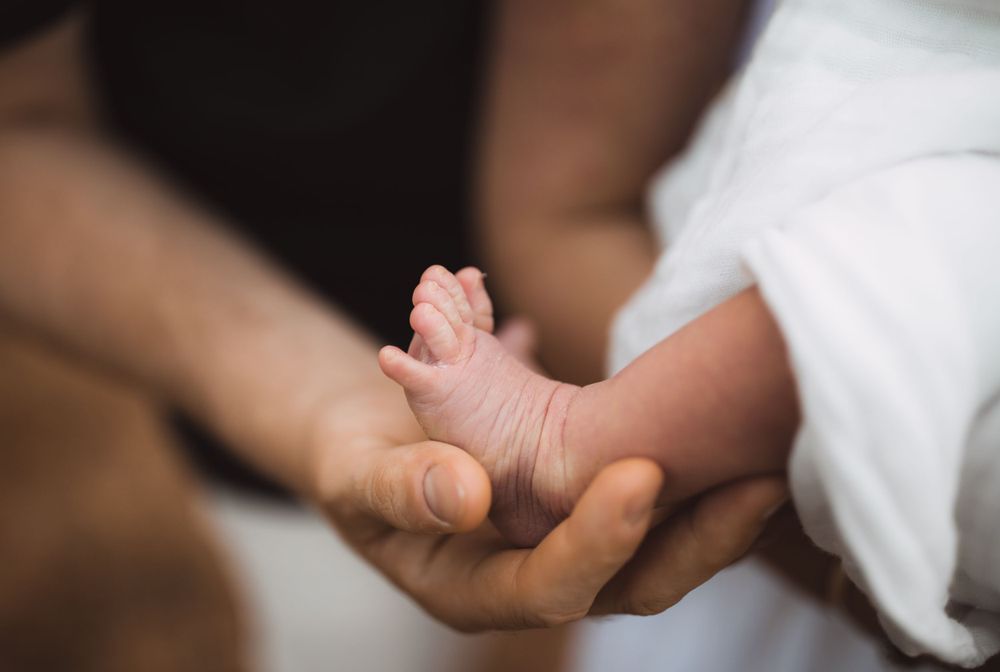Close-up of a tiny newborn baby's foot being gently held in an adult's hand.
