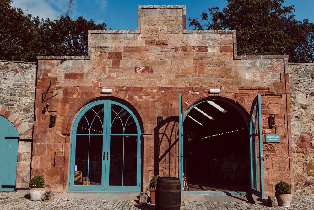 Exterior view of rustic stone wedding venue with arched windows and blue sky.