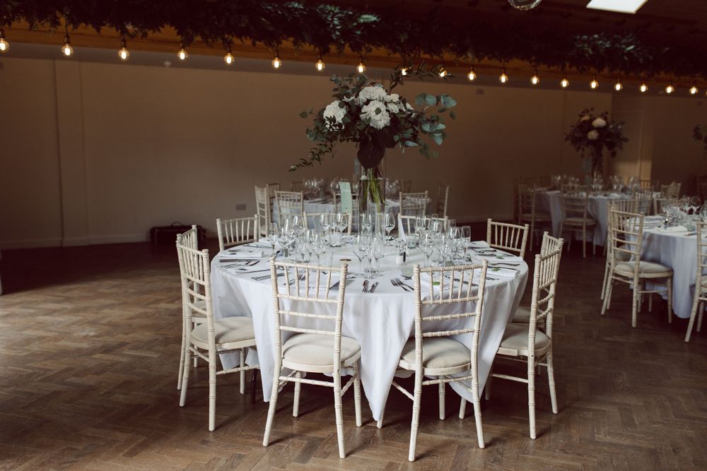 Wedding reception tables arranged with white linens and chiavari chairs under ambient lighting.