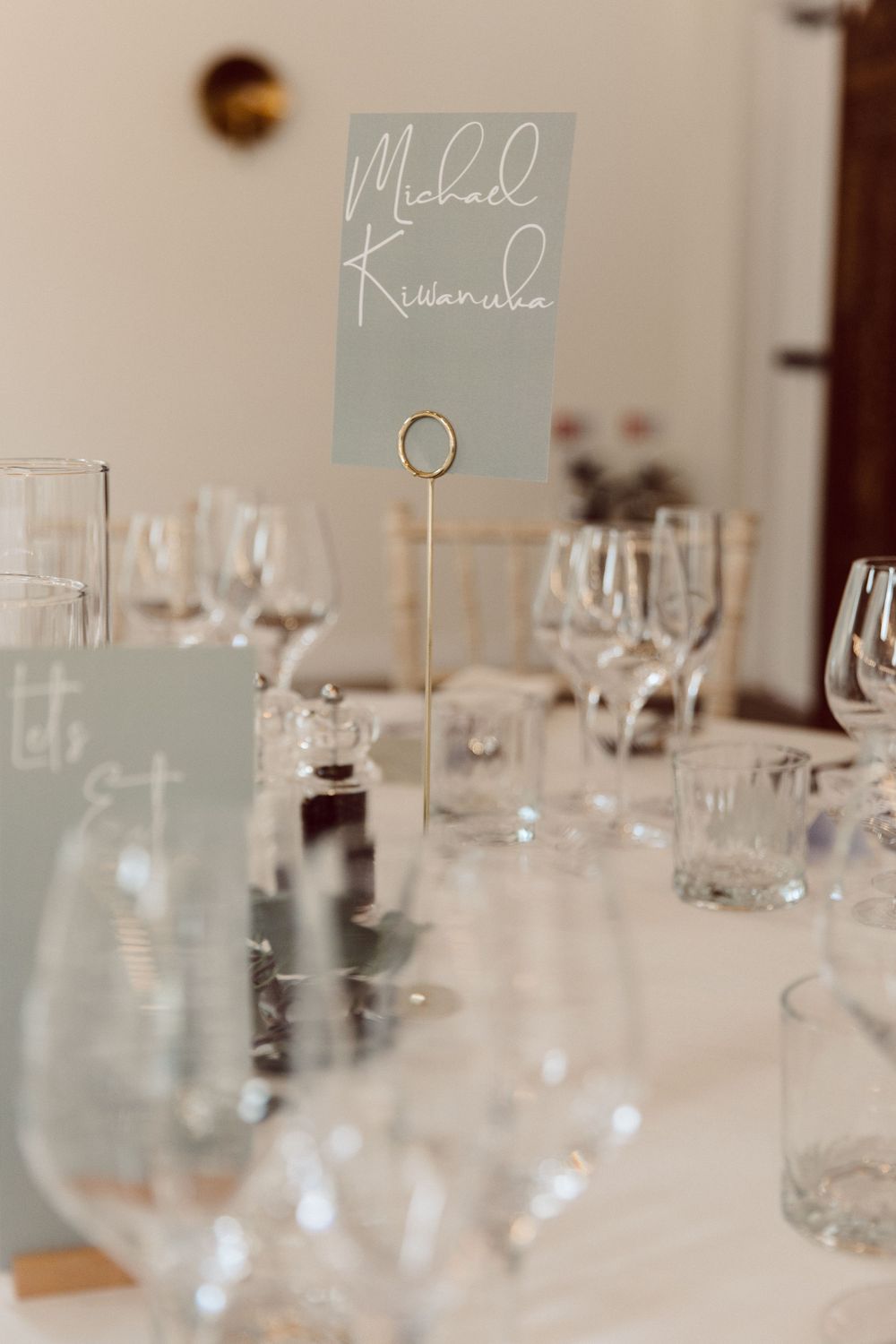 Wedding table settings with sage green place cards and crystal glassware.