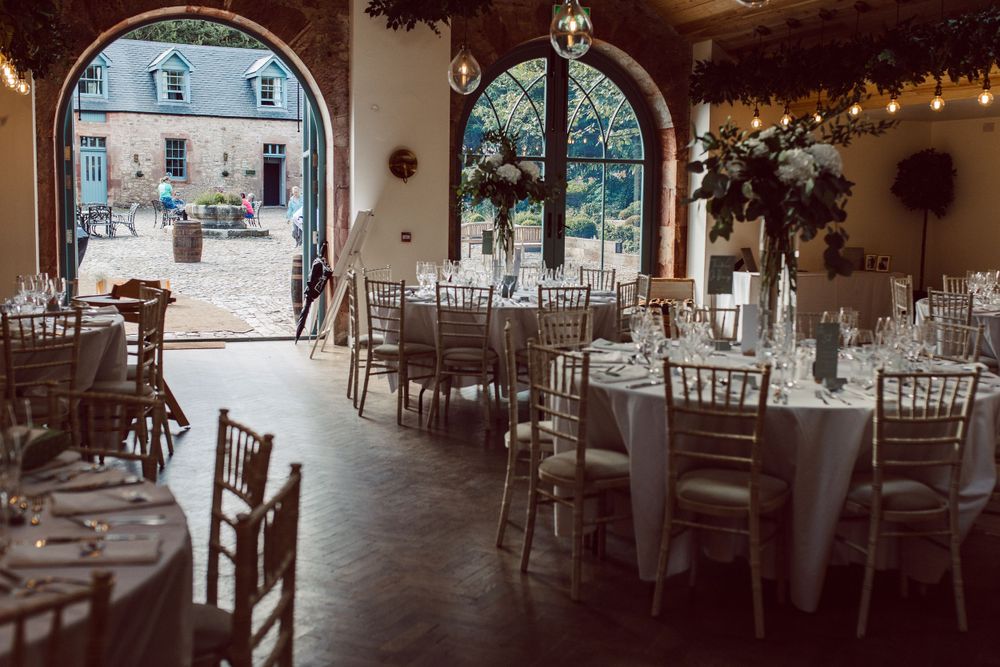 Elegant wedding reception venue with white chairs and tables arranged under string lights and floral decor.