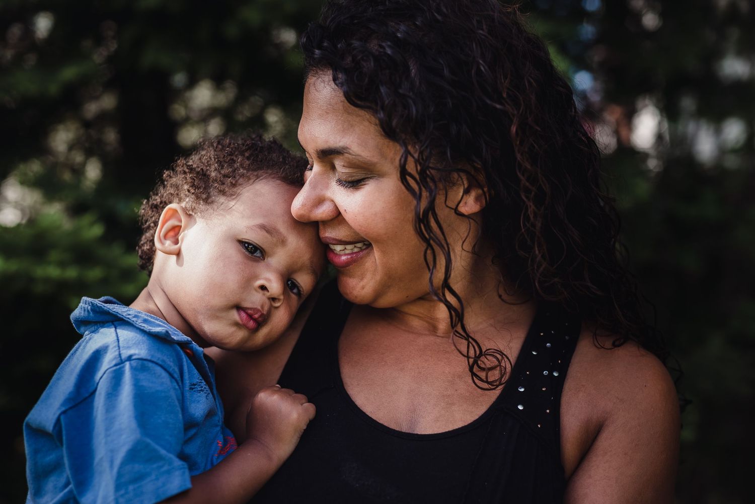 A woman holds her young son and smiles down at him as he looks toward the camera.