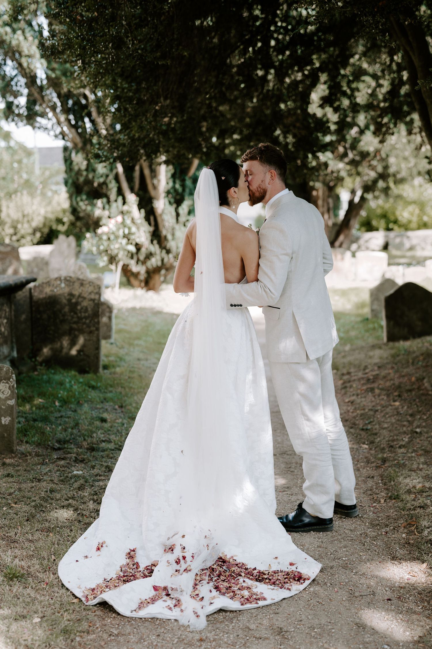 bride and groom kissing with confetti petals all over the wedding dress train outside st Nicholas church in Oxfordshire