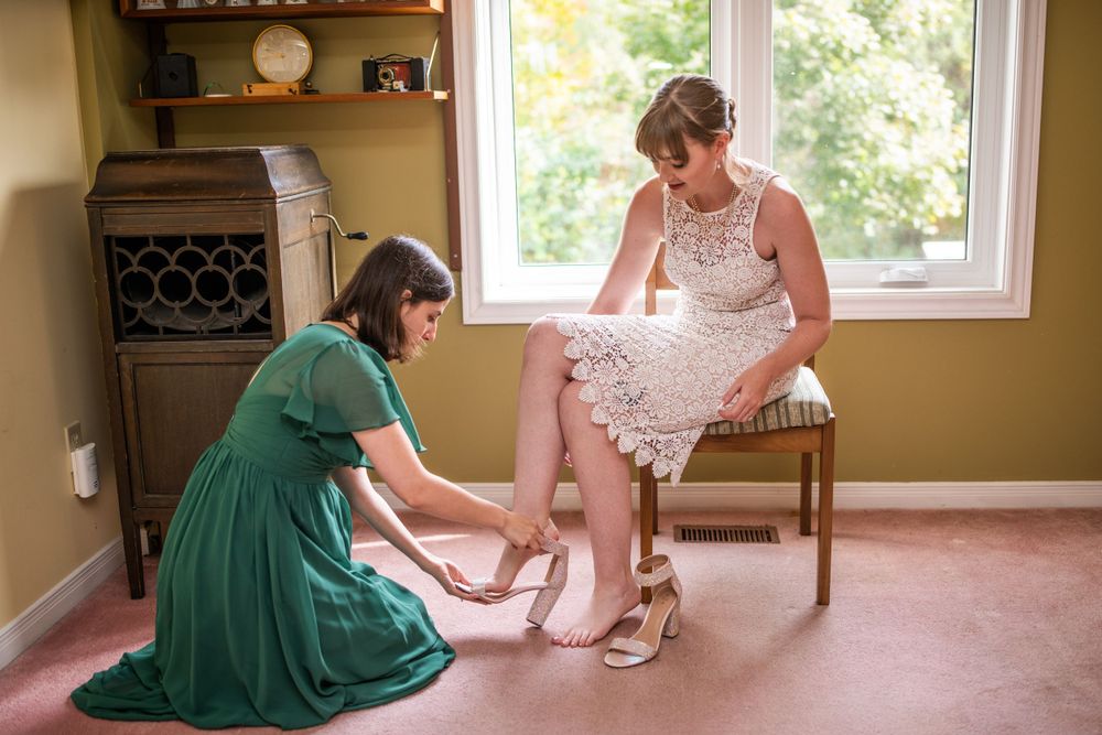 maid of honour putting shoes on bride before wedding ceremony