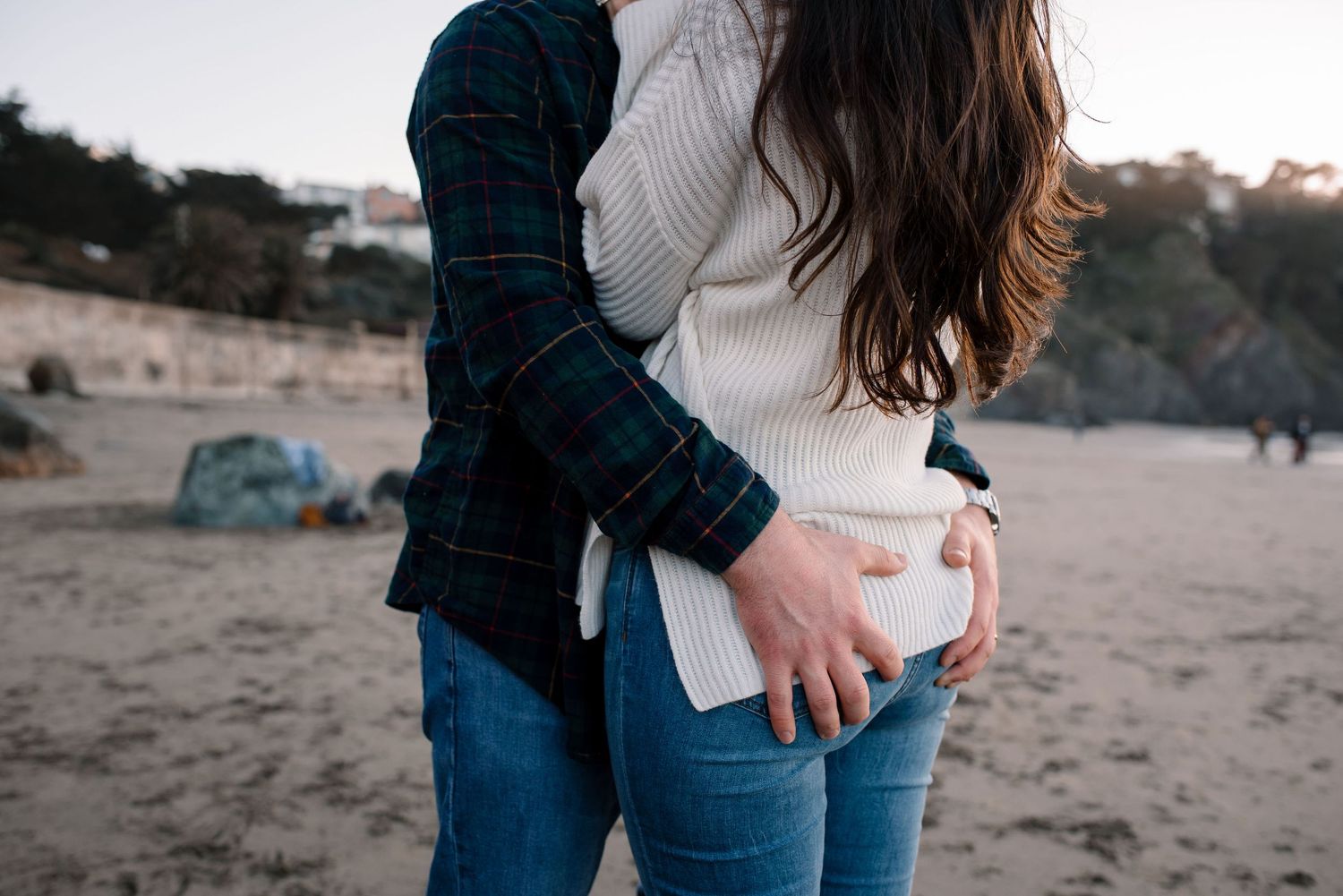 Two people hold hands while walking along a scenic beach at sunset.